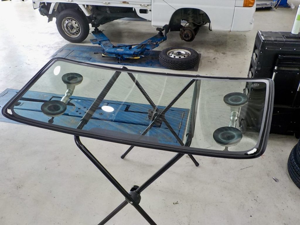 伊賀市のモリタ自動車：作業台に載せられた交換用の新品フロントガラスと吸盤ツール（ガラス交換作業風景）